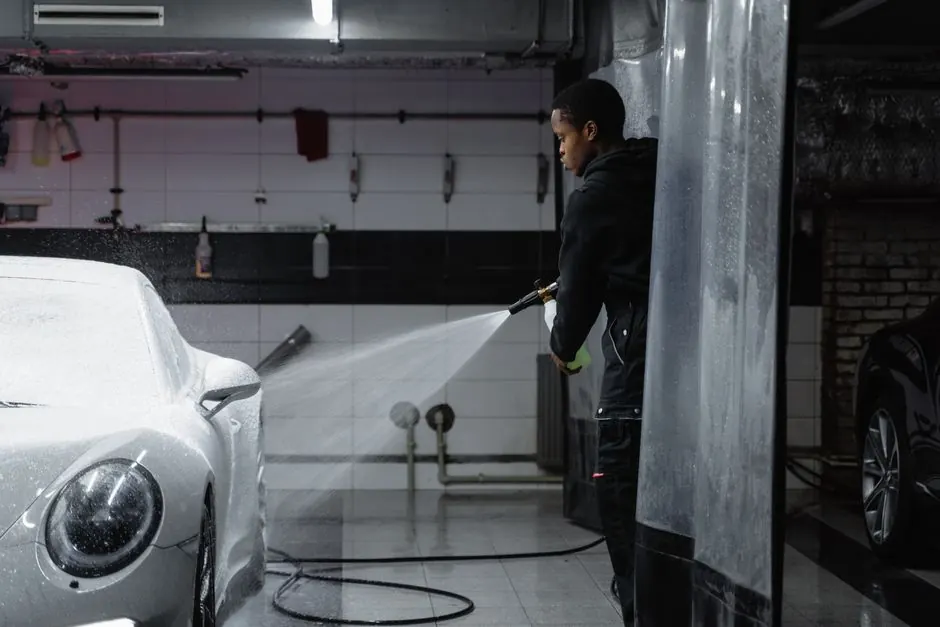 A person using a pressure washer to clean a car in an indoor garage setting.