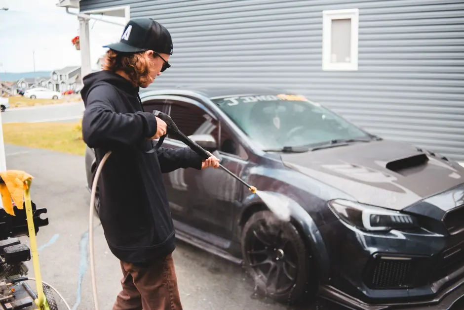 Back view of faceless worker using hosepipe while washing expensive black luxury sports car in daytime