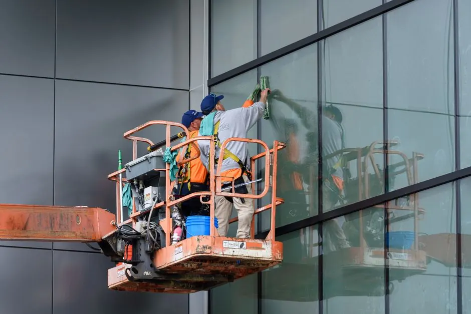 Window cleaners working on a skyscraper using a hydraulic lift in urban setting.